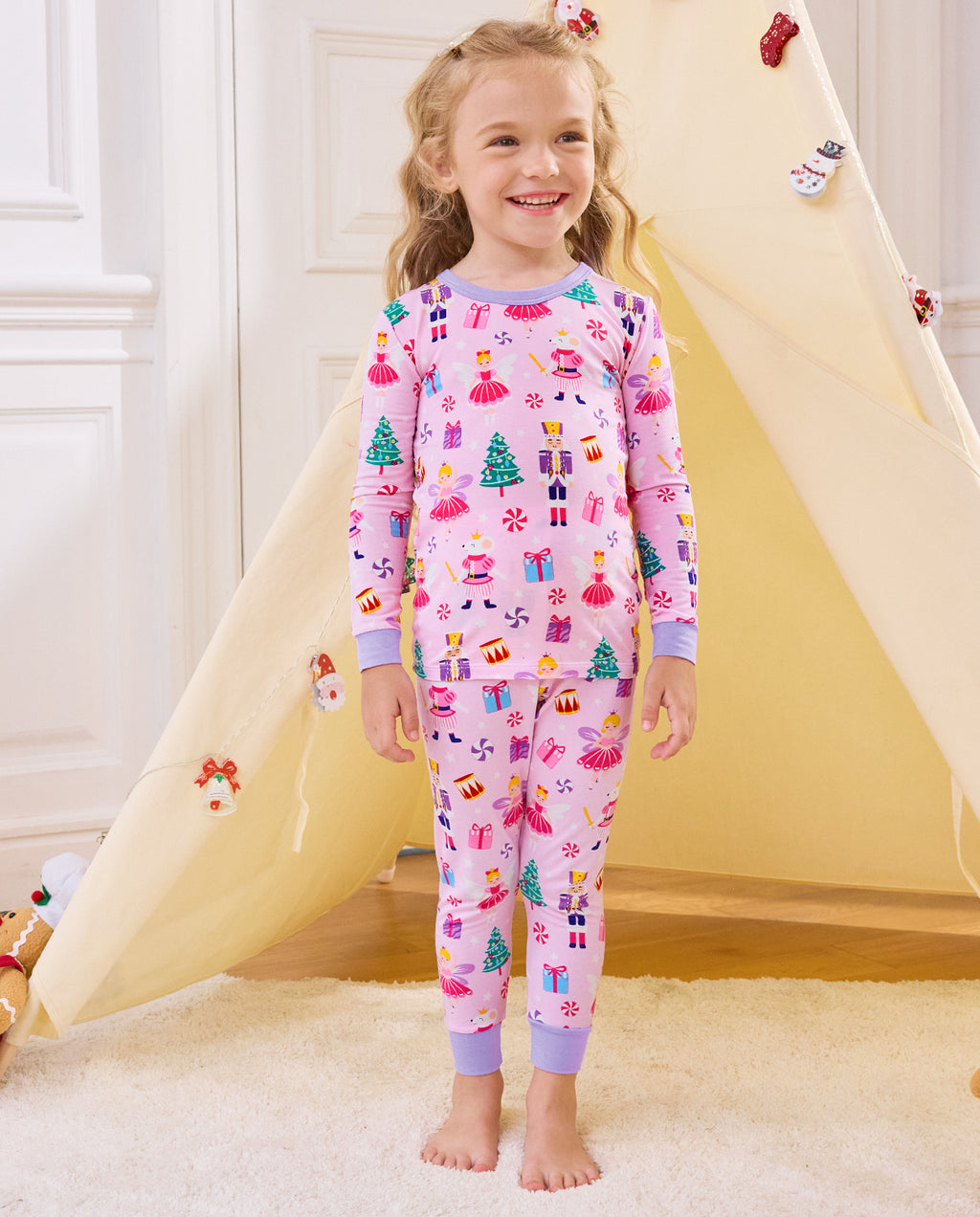 Child standing by a play tent in Nutcracker Fairy pajamas with lavender cuffs.