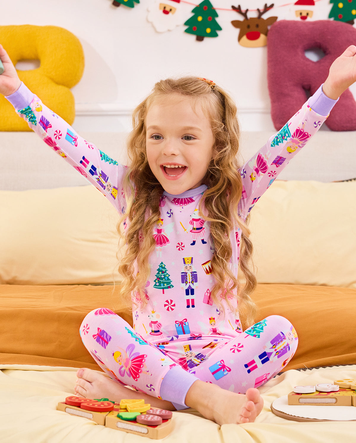 Child seated on a sofa with a wand and arms raised in Nutcracker Fairy pajamas.