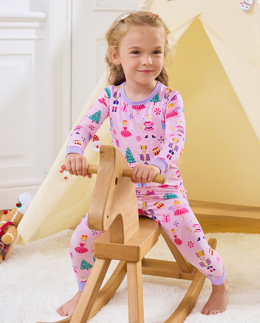 Child seated on a wooden rocking horse in Nutcracker Fairy pajamas.