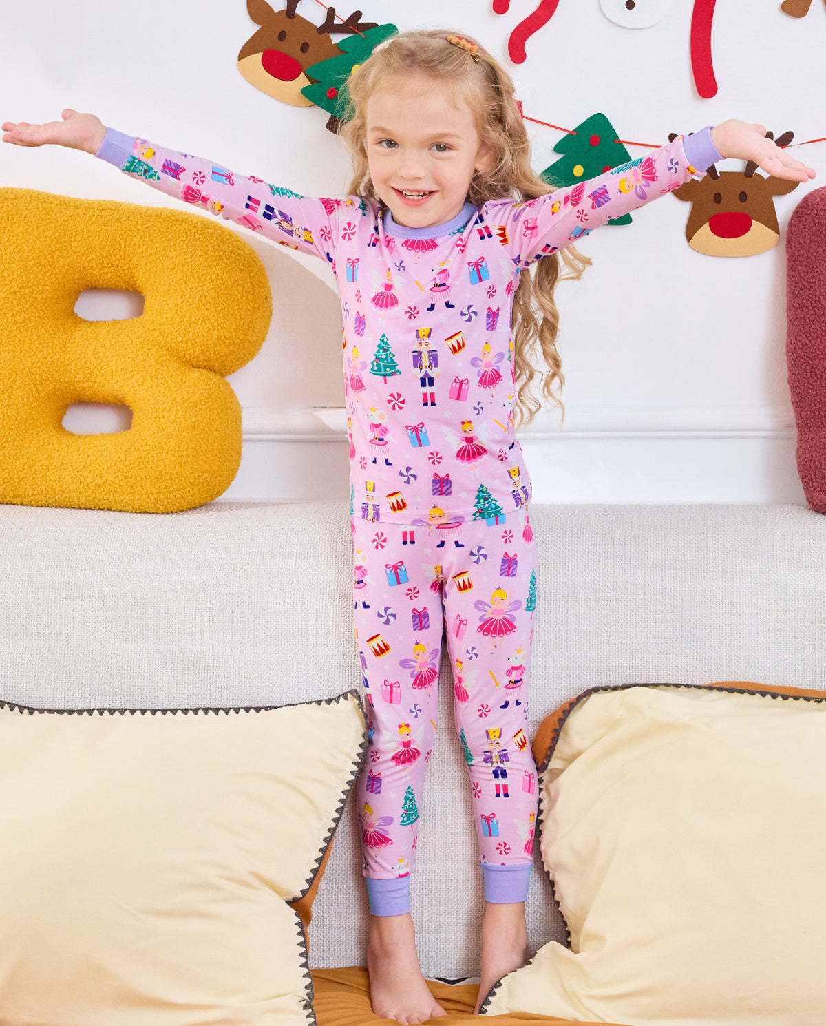 Child seated on a sofa with arms out in Nutcracker Fairy pajamas.