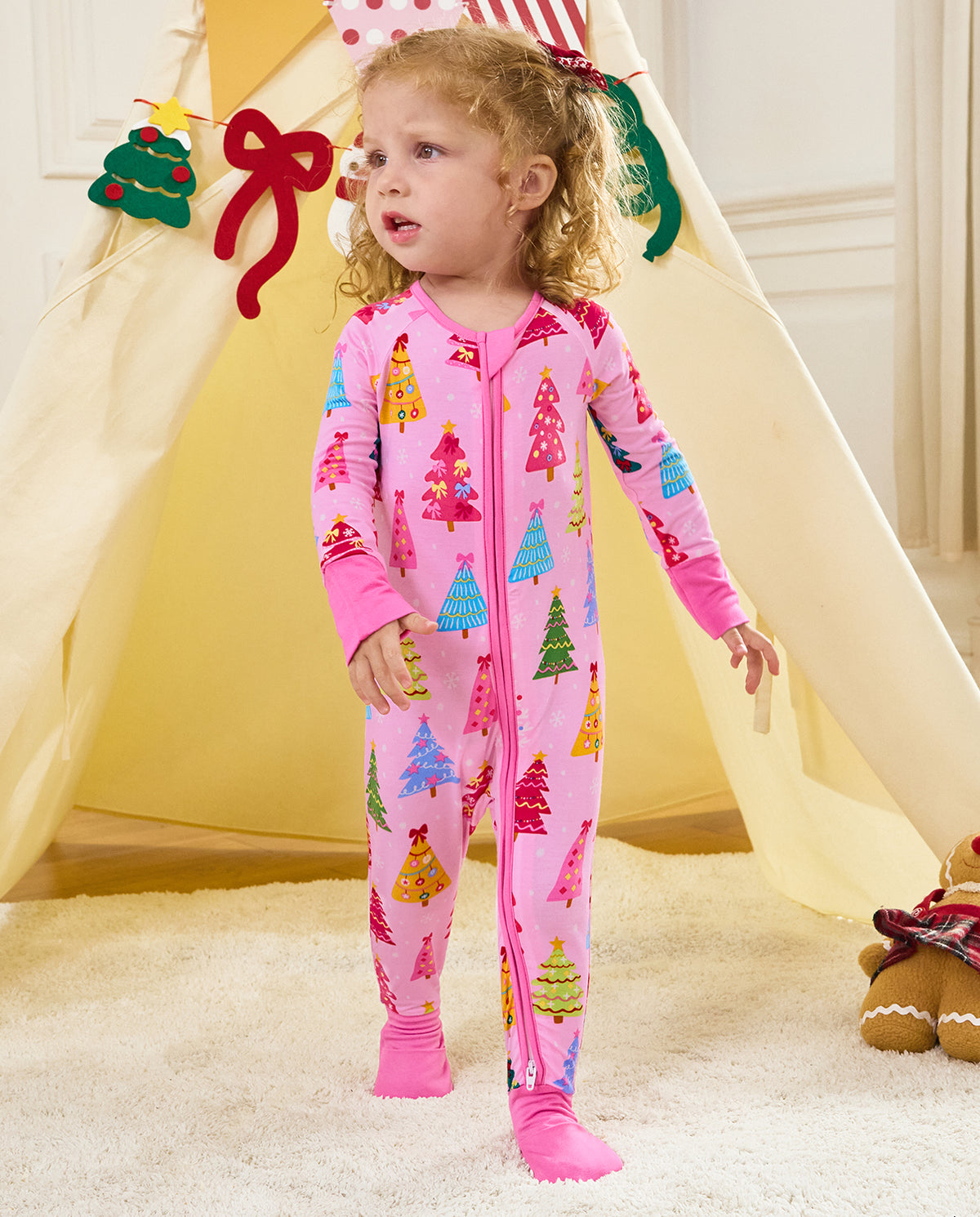 Child standing by a holiday play tent in the pink Pastel Christmas zip-up romper.