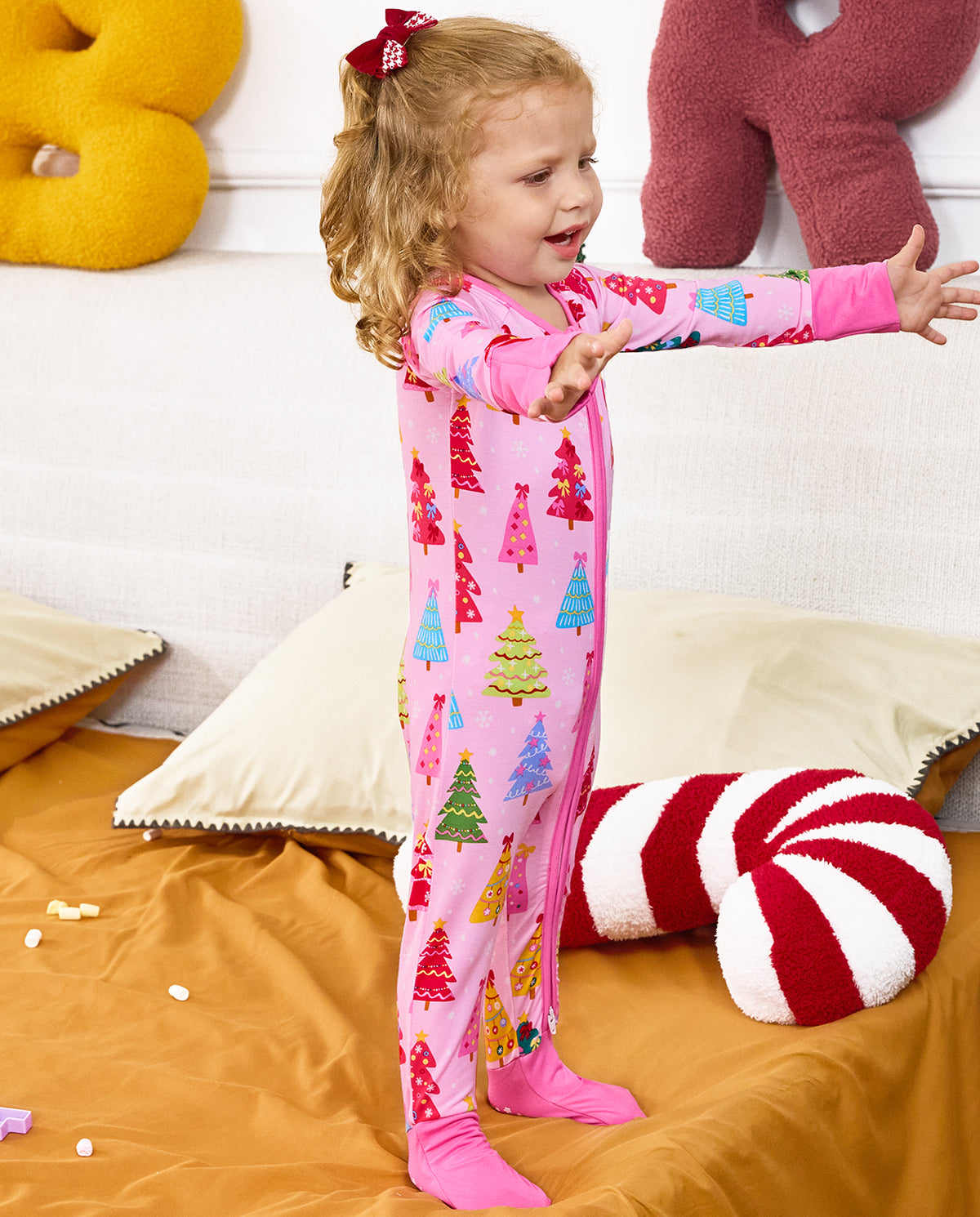 Child seated on orange bedding with arms out in the Pastel Christmas romper.