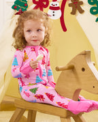 Child seated holding a toy beside a wooden rocking horse in the Pastel Christmas romper.