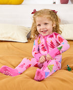 Child seated on bedding and smiling in the pink Pastel Christmas romper.
