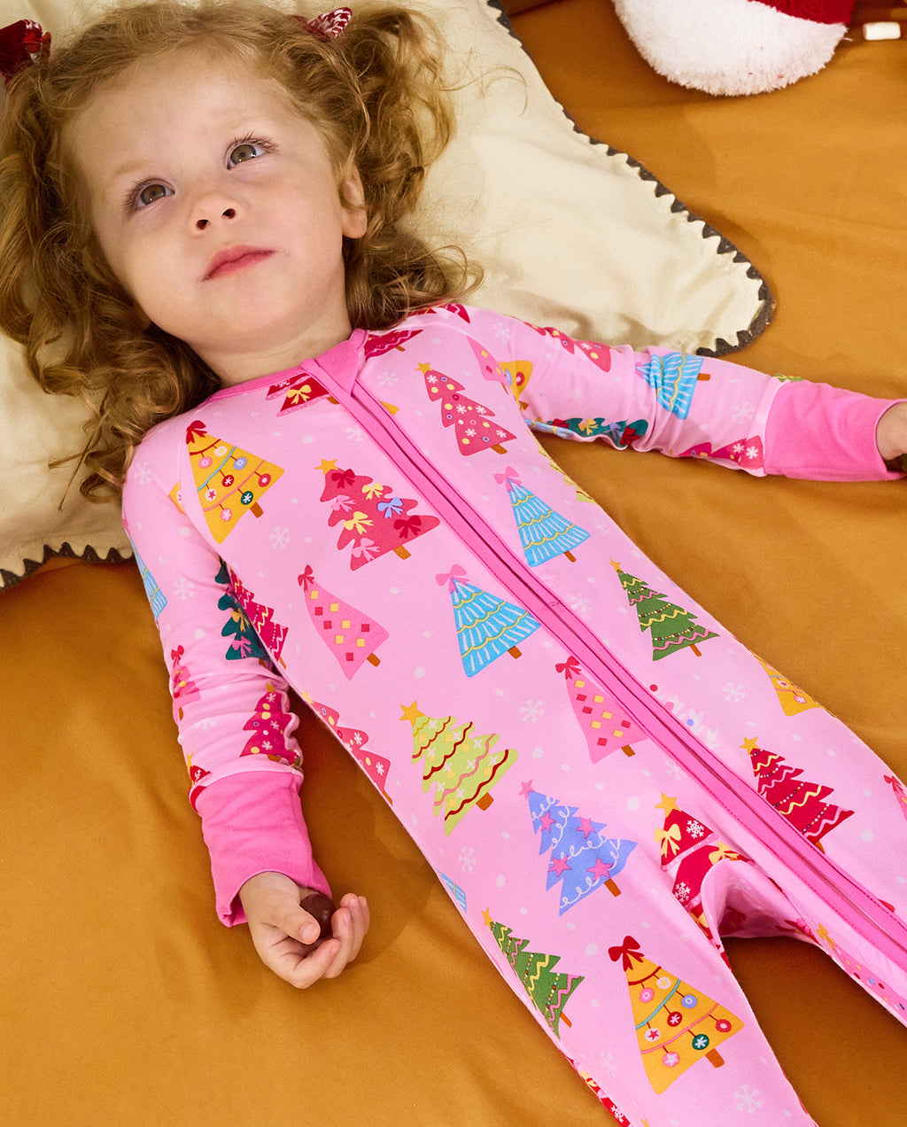 Child lying on orange bedding in the Pastel Christmas zip-up romper.