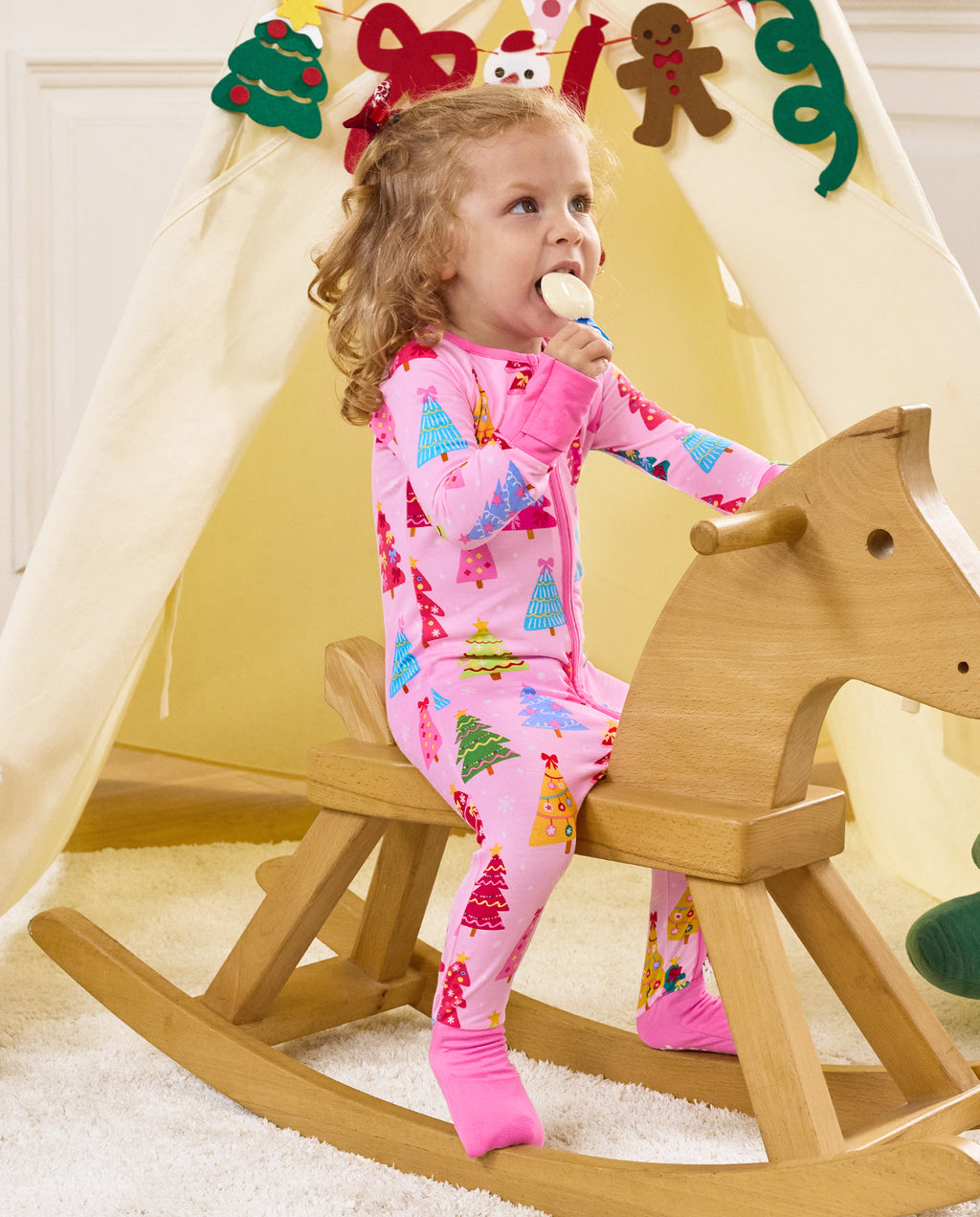 Child seated on a wooden rocking horse holding a toy in the Pastel Christmas romper.