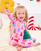 Child seated on bedding with a hand raised in Pastel Christmas pajamas.