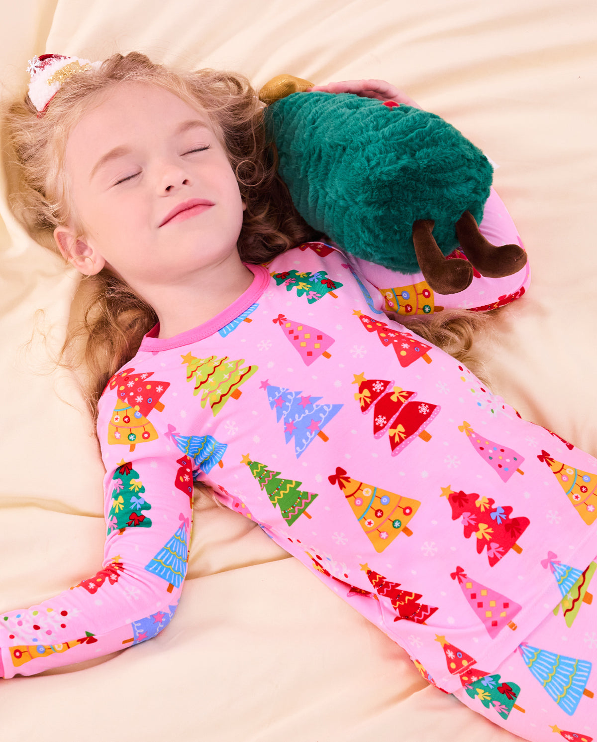 Child reclining on bedding with a plush tree in Pastel Christmas pajamas.