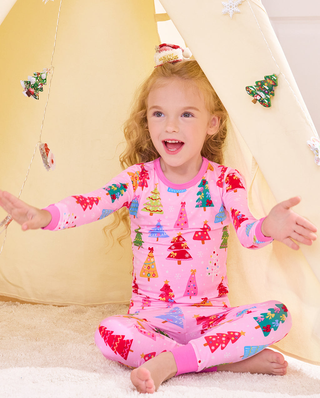 Child seated cross-legged by a holiday play tent in the Pastel Christmas pajama set.