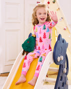 Child seated on a slide with a plush tree in Pastel Christmas pajamas.