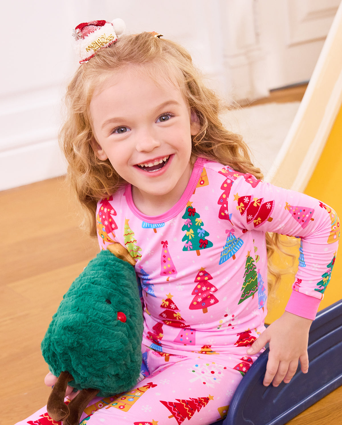 Close-up of a smiling child seated on a slide in the Pastel Christmas long-sleeve top.