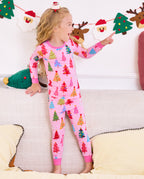 Child standing on a sofa and pointing at a holiday garland in Pastel Christmas pajamas.