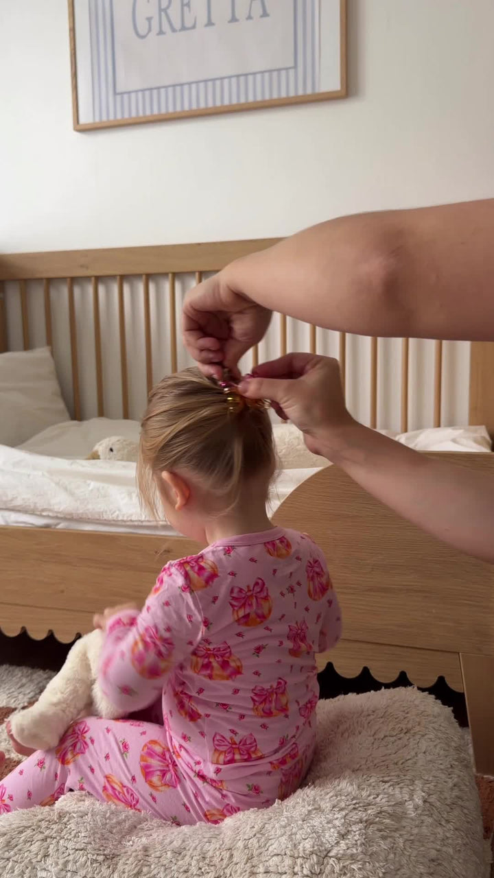 A child getting ready for the day in pink holiday-print Babee Reshinee pajamas.