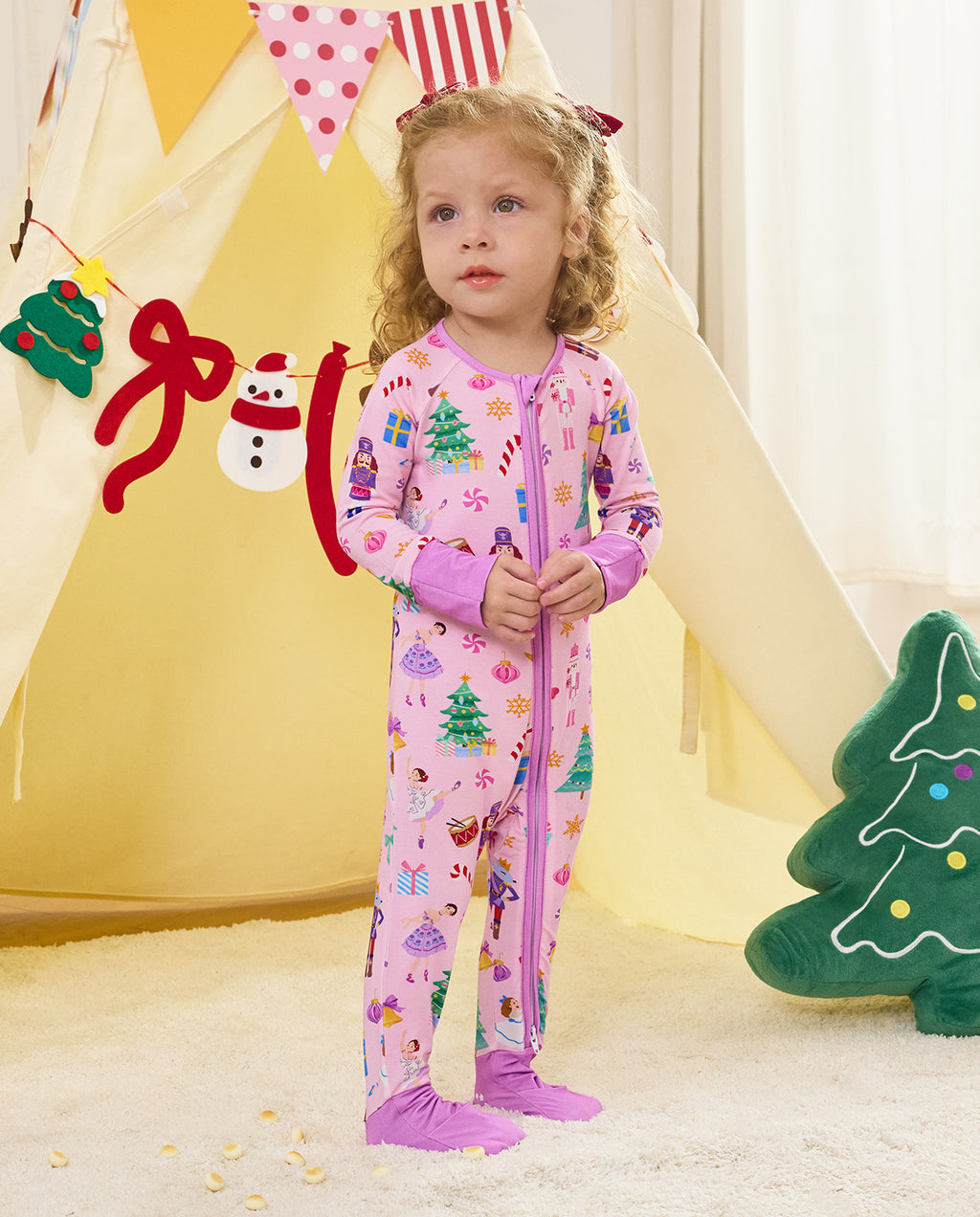 Child standing by a play tent in the Pink Nutcracker romper with covered feet.