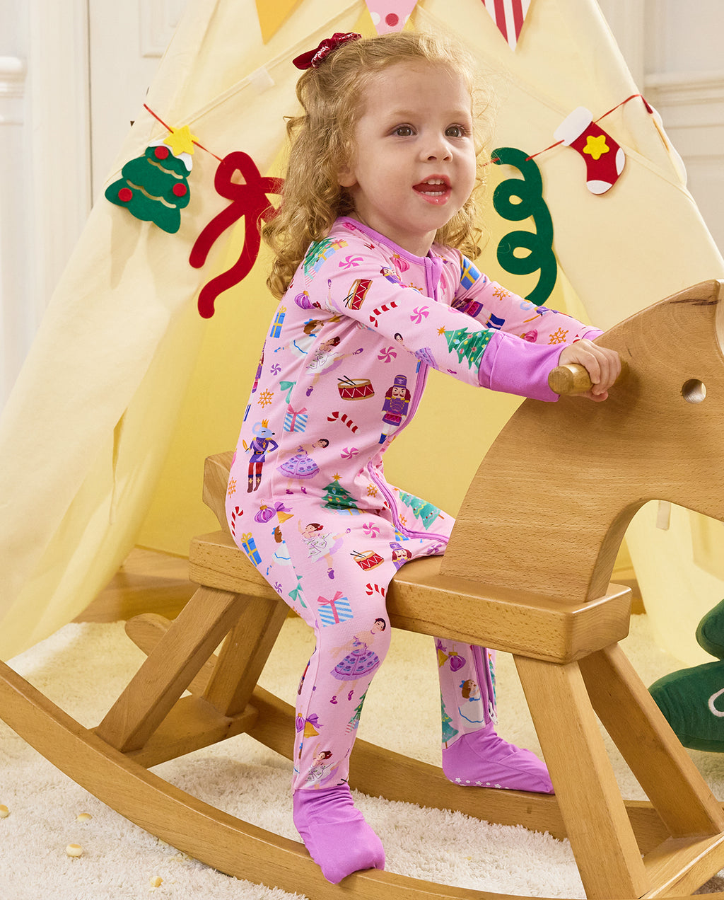 Child seated on a wooden rocking horse in the Pink Nutcracker romper.