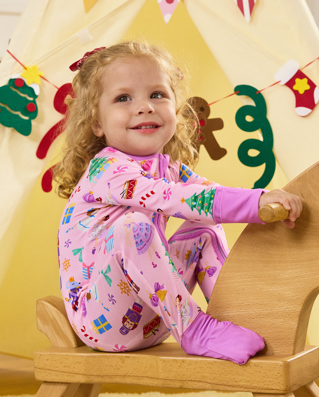 Close view of a child seated on a wooden rocking horse in the Pink Nutcracker romper.