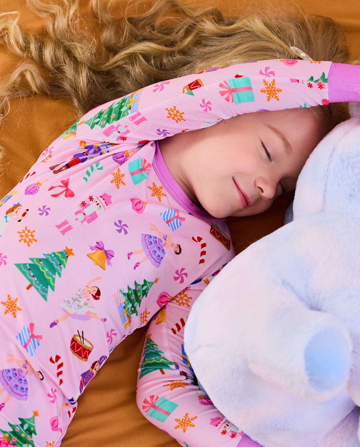 Child resting on bedding with an arm over the head in Pink Nutcracker pajamas.