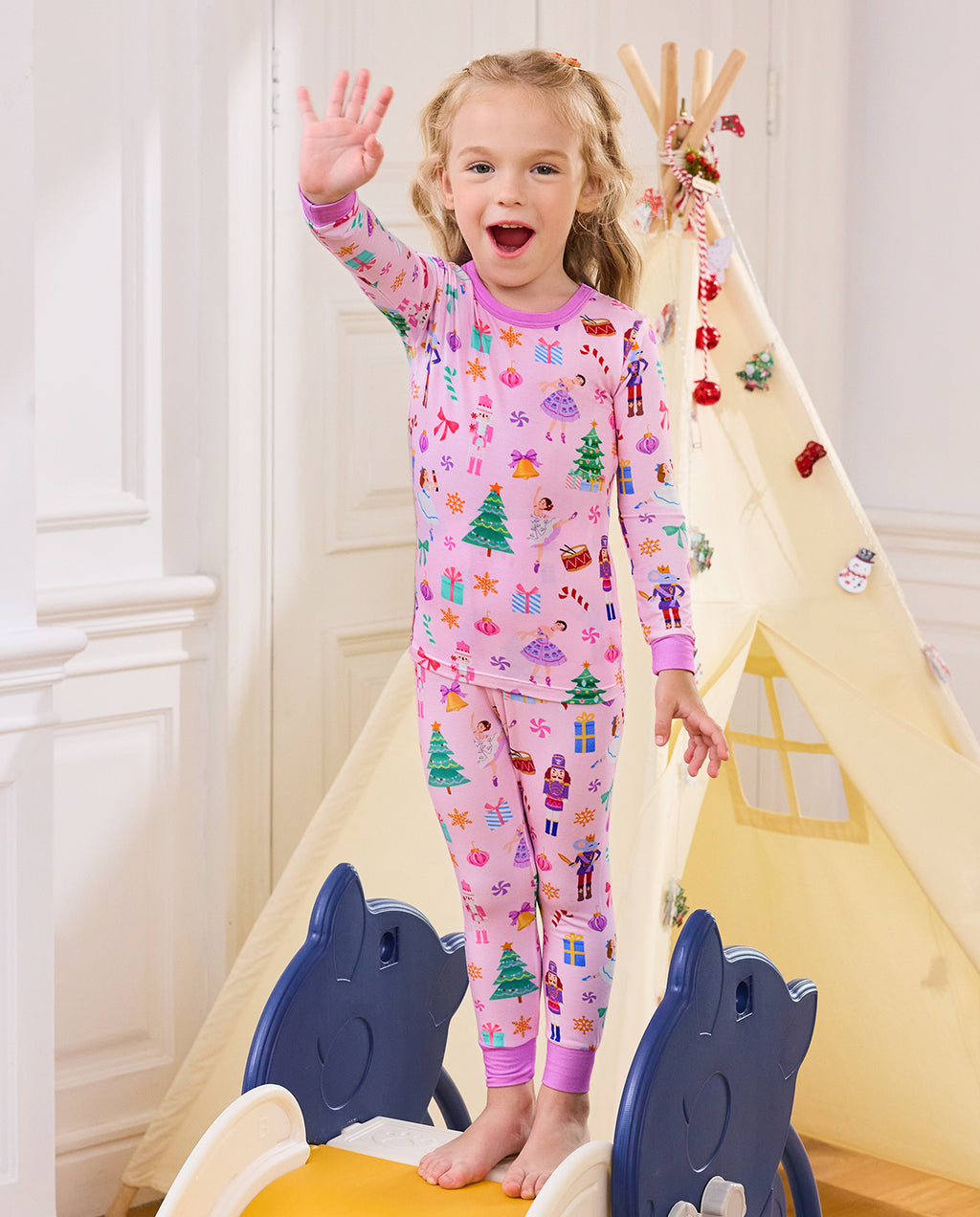 Child standing on a slide and waving in Pink Nutcracker pajamas.