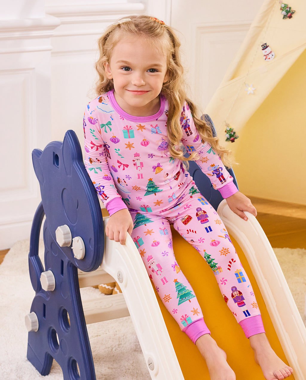 Child seated on a slide in Pink Nutcracker pajamas.