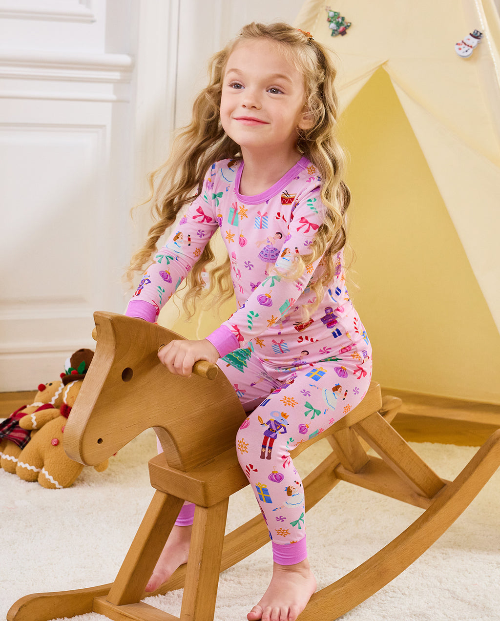 Child seated on a wooden rocking horse in Pink Nutcracker pajamas.