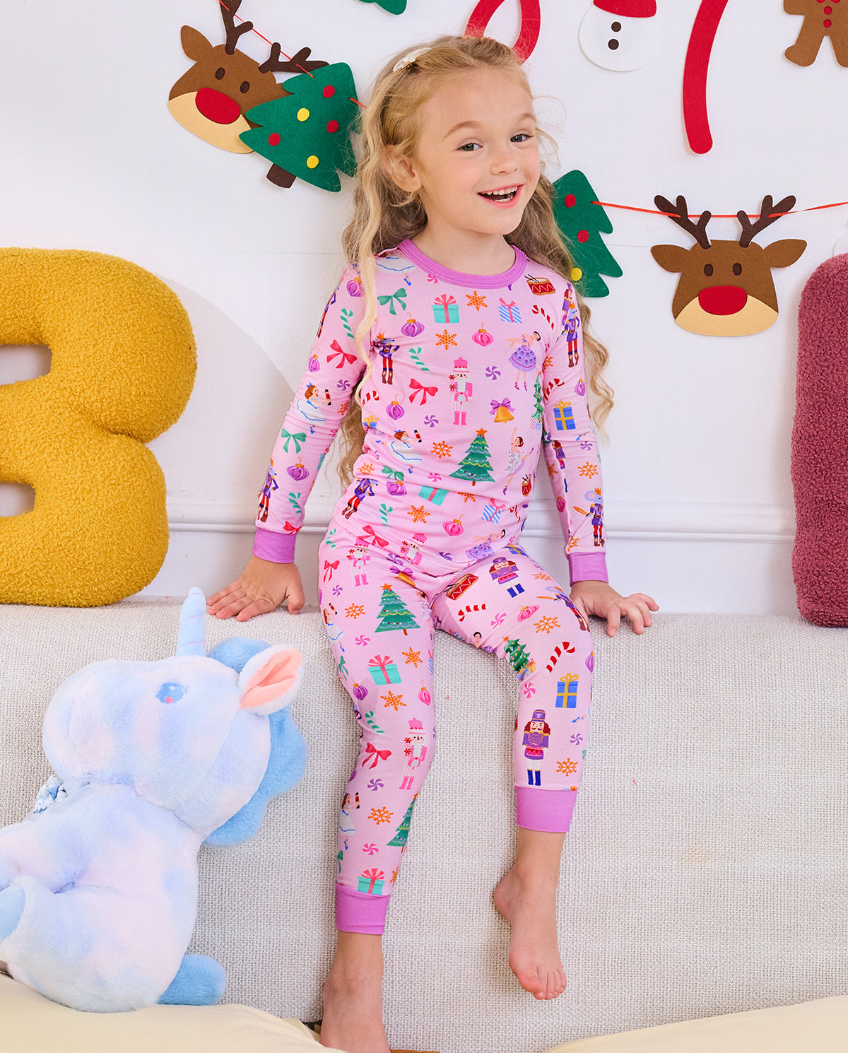 Child seated on a sofa beside a unicorn plush in Pink Nutcracker pajamas.