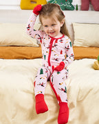 Child seated on bedding with a covered hand raised in the Pink Penguins romper.