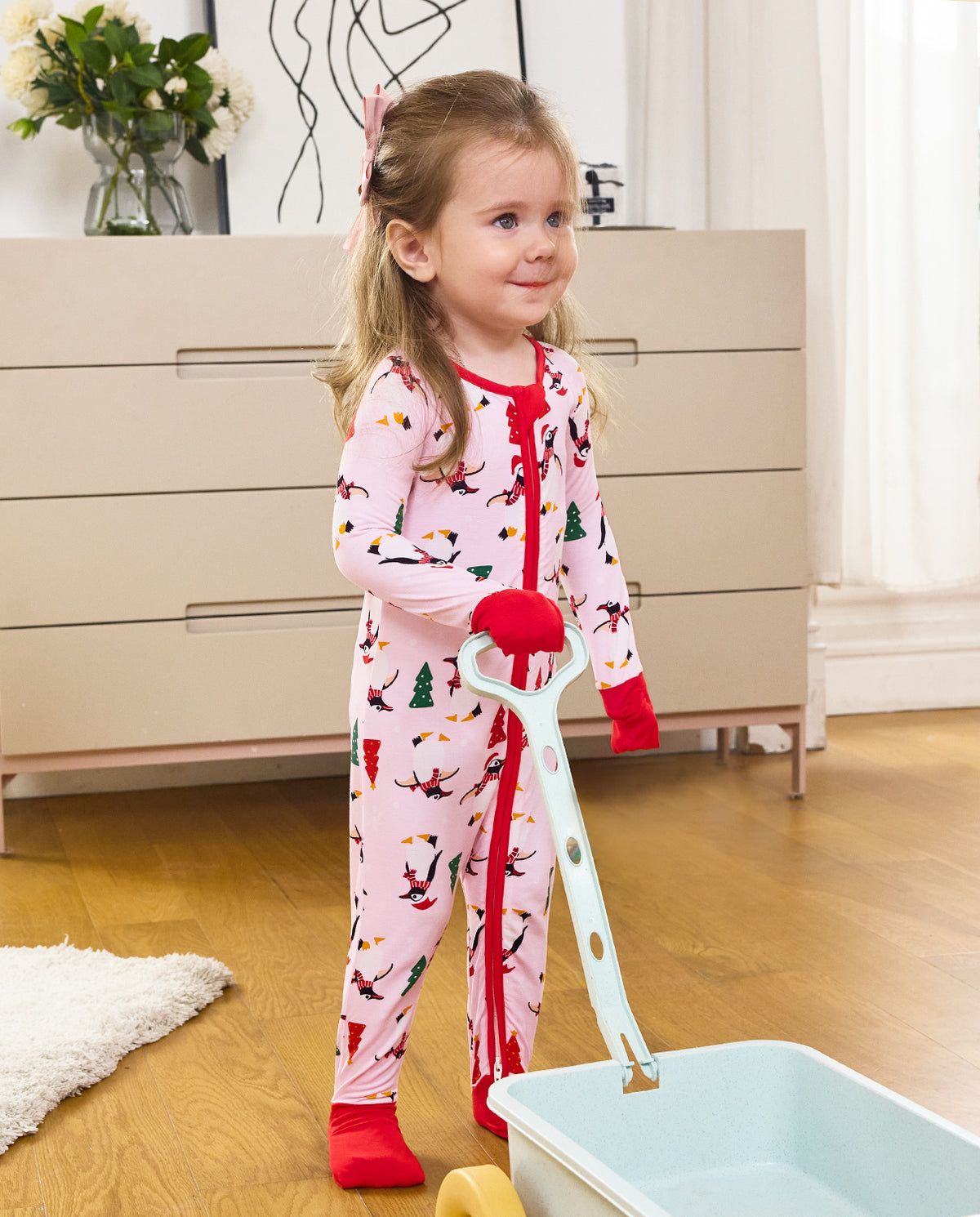Child standing beside a pale blue cart in the Pink Penguins zip-up romper.
