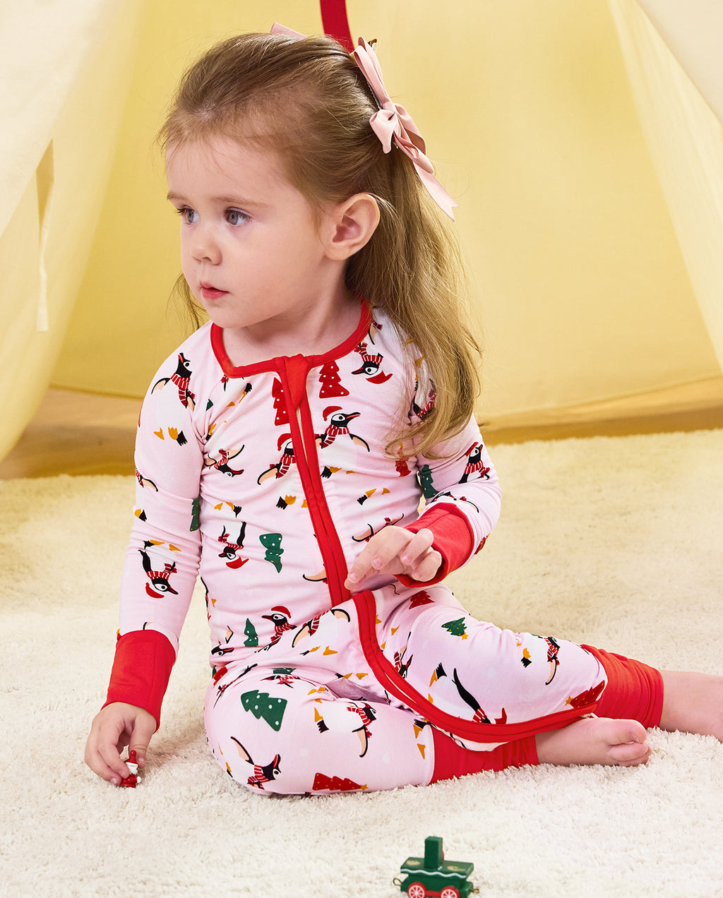 Child seated by a play tent in the Pink Penguins romper.