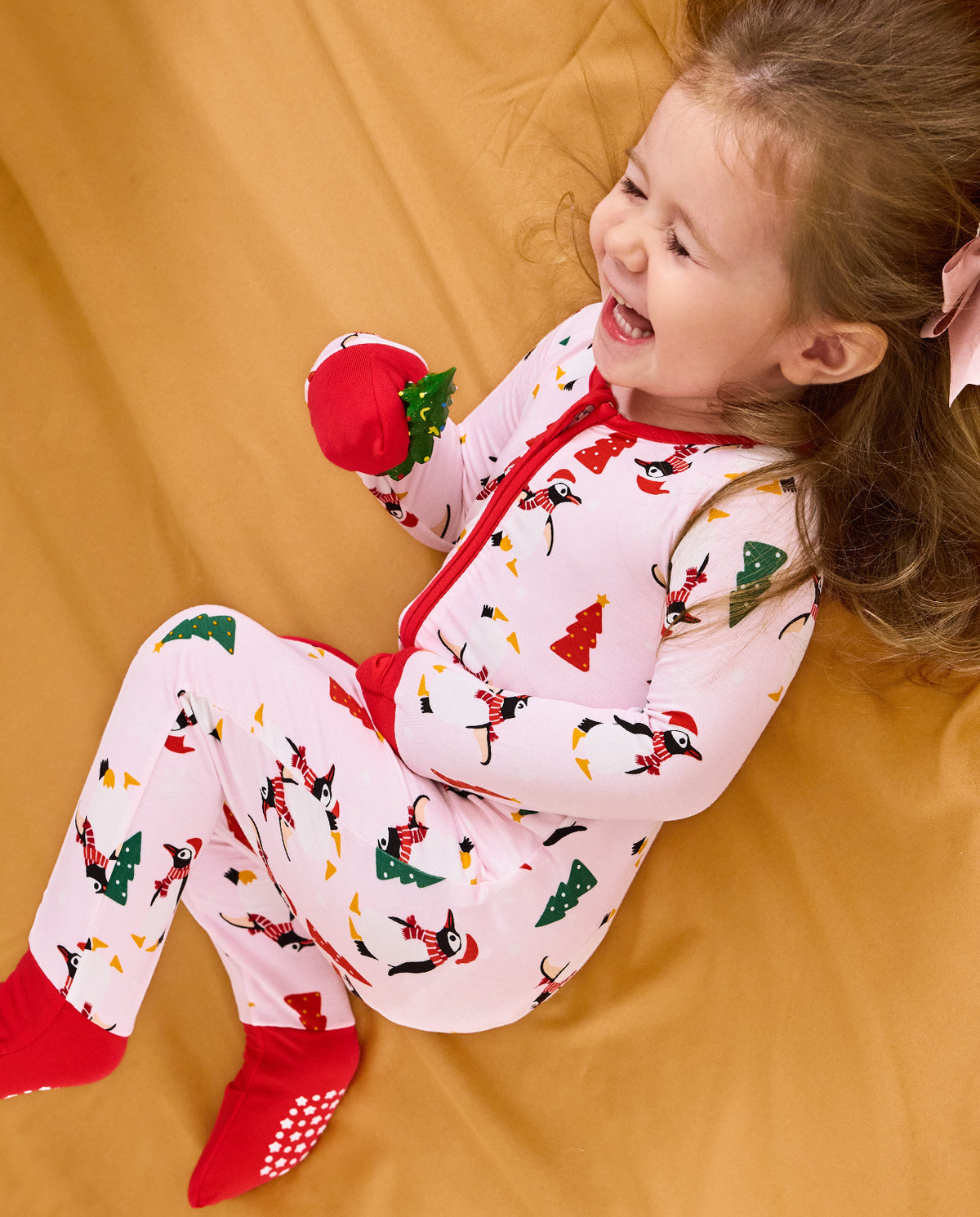 Child reclining on orange bedding smiling in the Pink Penguins romper.