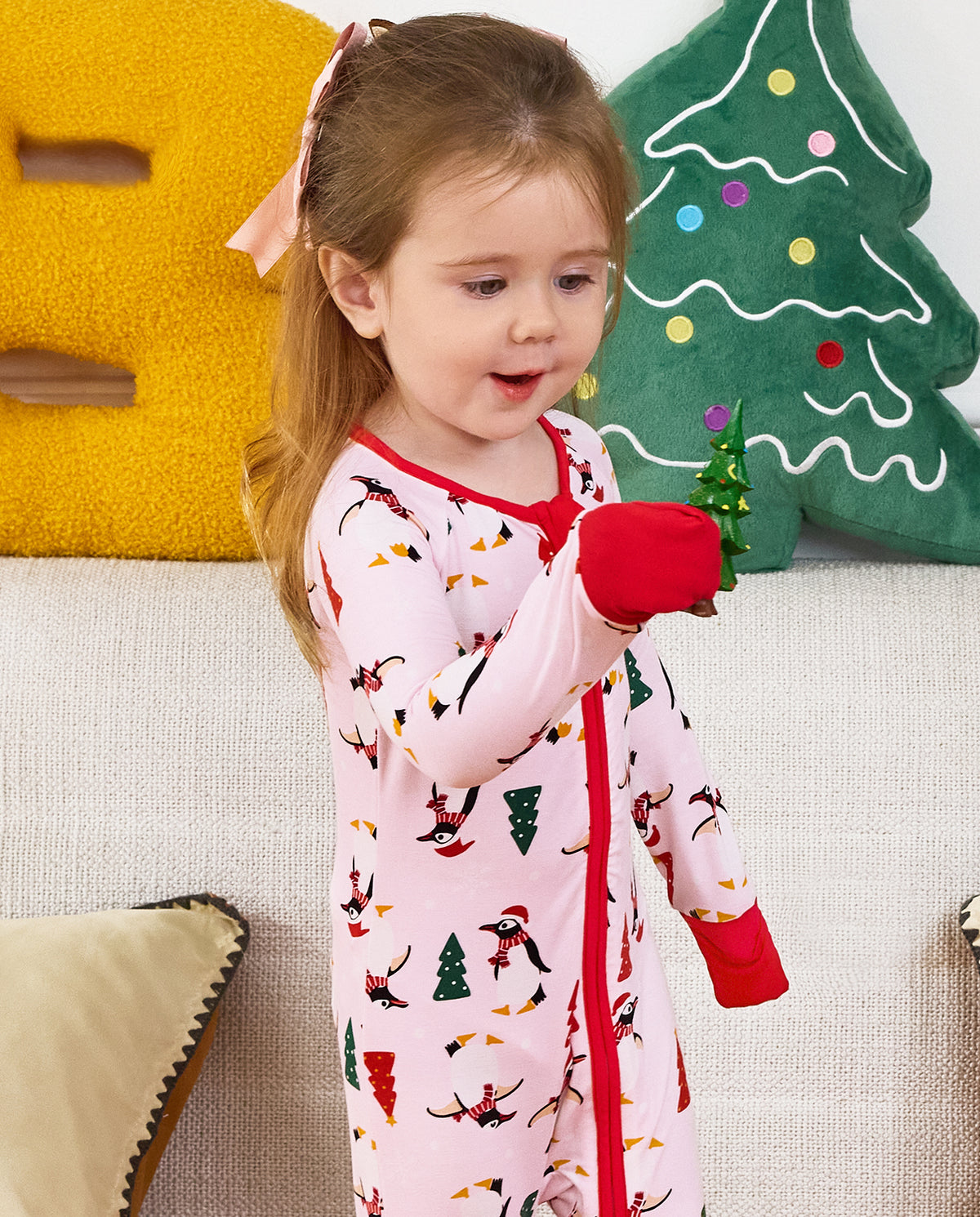 Child holding a small toy while standing in the Pink Penguins zip-up romper.