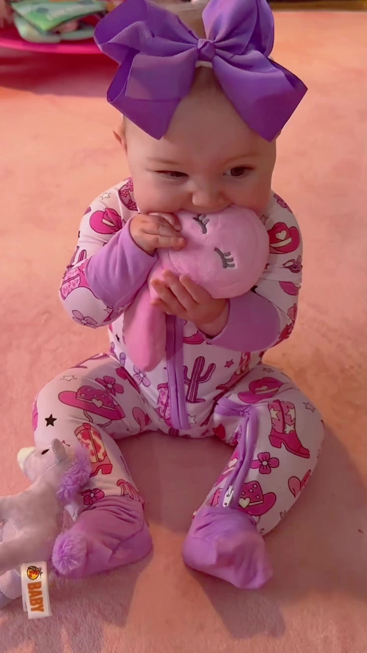 A baby wearing a pink western-print Babee Reshinee zip-up outfit with purple cuffs.
