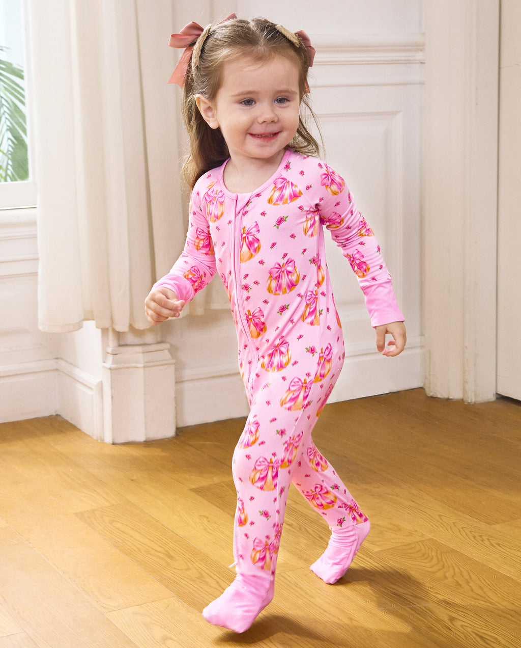 Smiling child walking in the Pumpkin Bows zip-up romper with pink cuffs.