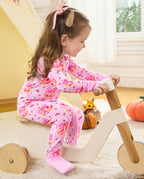 Side view of a child seated on a wooden tricycle wearing the Pumpkin Bows romper.