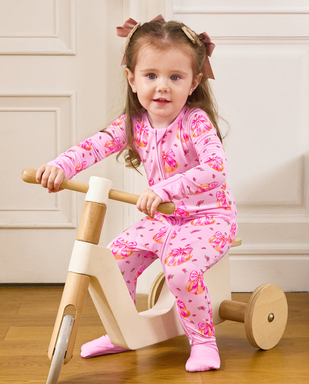 Front view of a child seated on a wooden tricycle in the Pumpkin Bows romper.