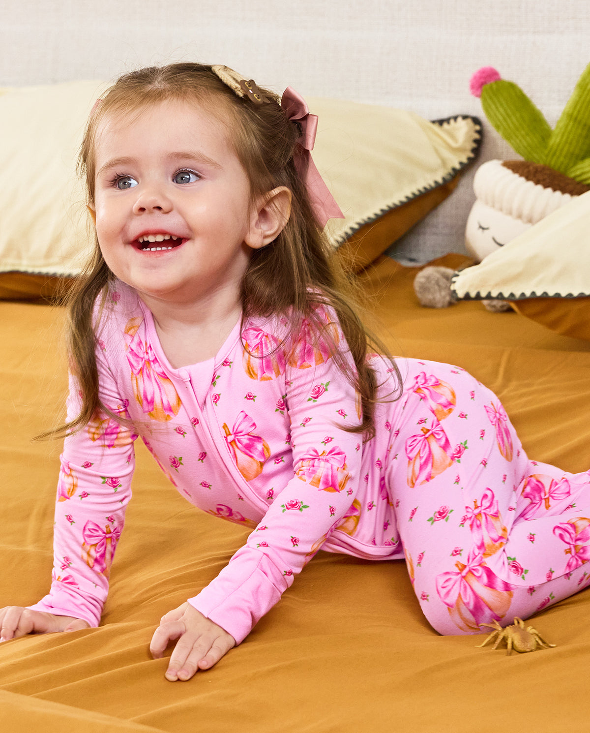 Child crawling on bedding in the pink Pumpkin Bows zip-up romper.