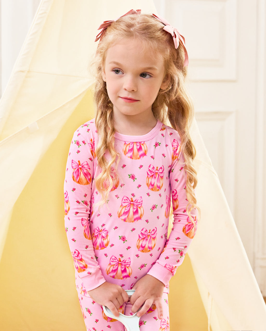 Child standing and looking aside in pink Pumpkin Bows long-sleeve pajamas.