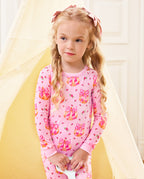 Child standing and looking aside in pink Pumpkin Bows long-sleeve pajamas.