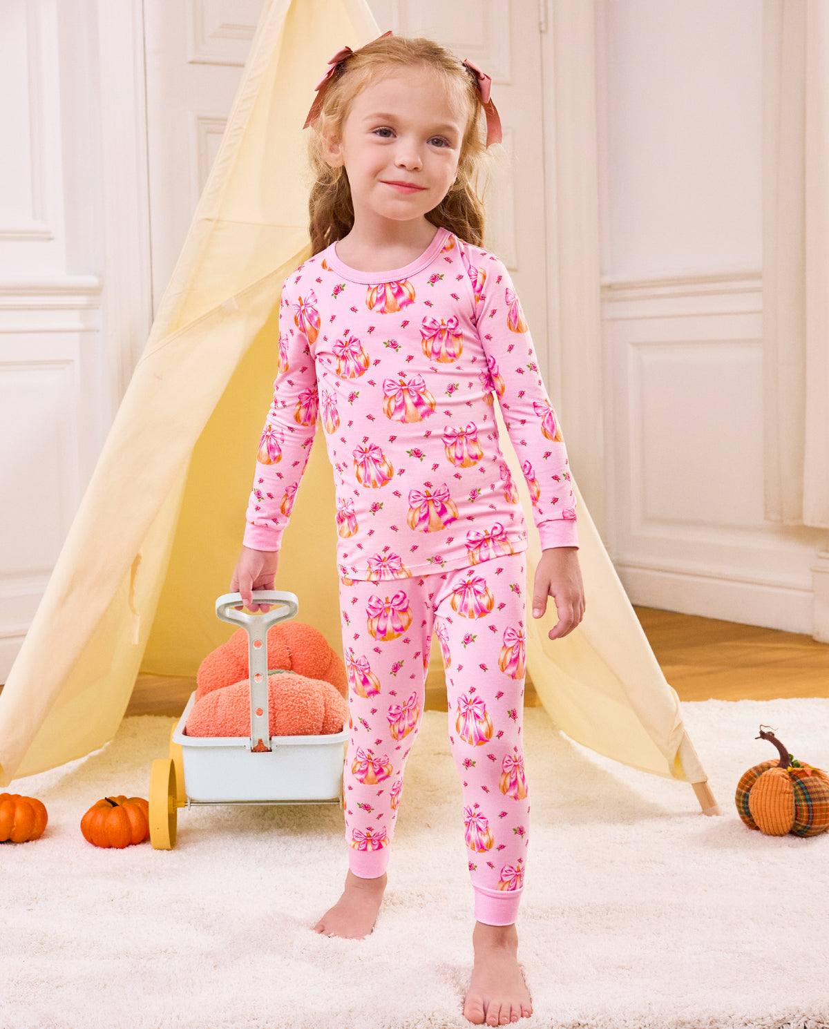Child standing beside a cart wearing the Pumpkin Bows pajama set.