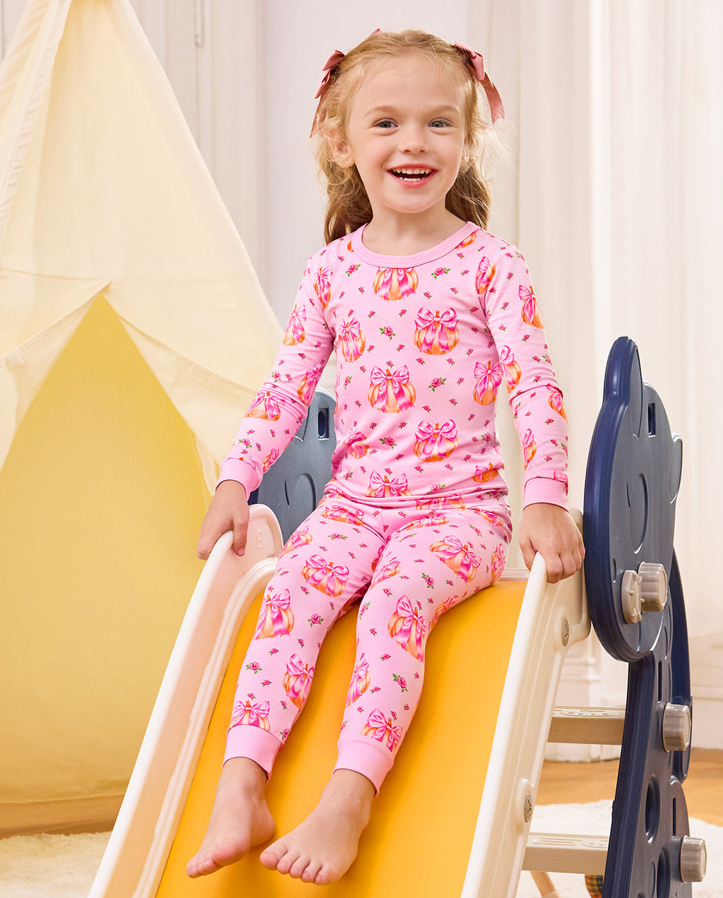 Smiling child seated on a slide in Pumpkin Bows pajamas.
