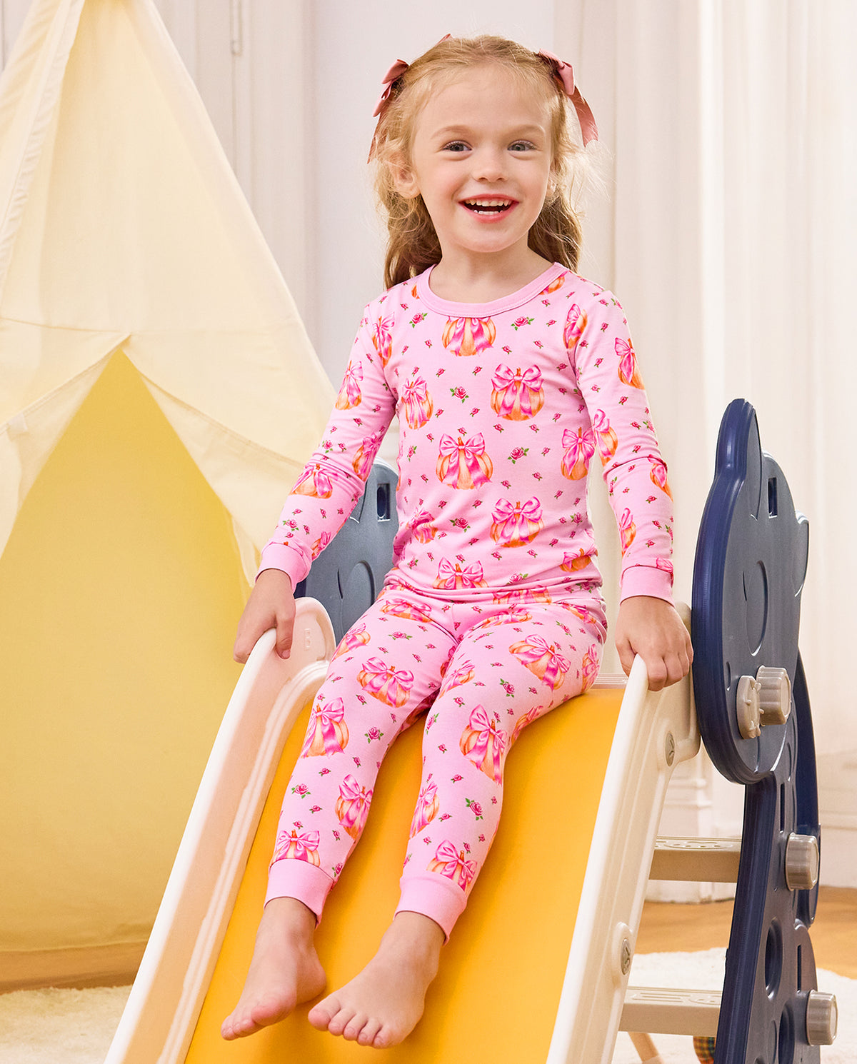 Smiling child seated on a slide in Pumpkin Bows pajamas.