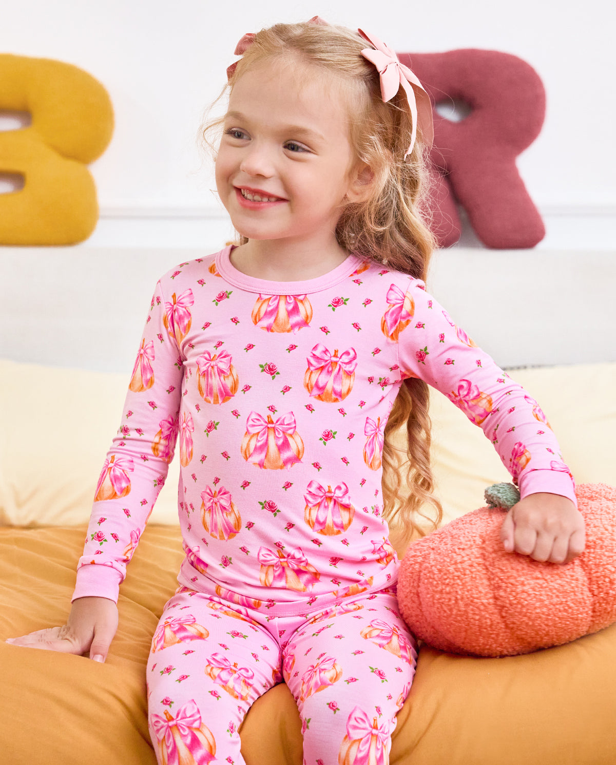 Child laughing and turning sideways on a sofa in Pumpkin Bows pajamas.