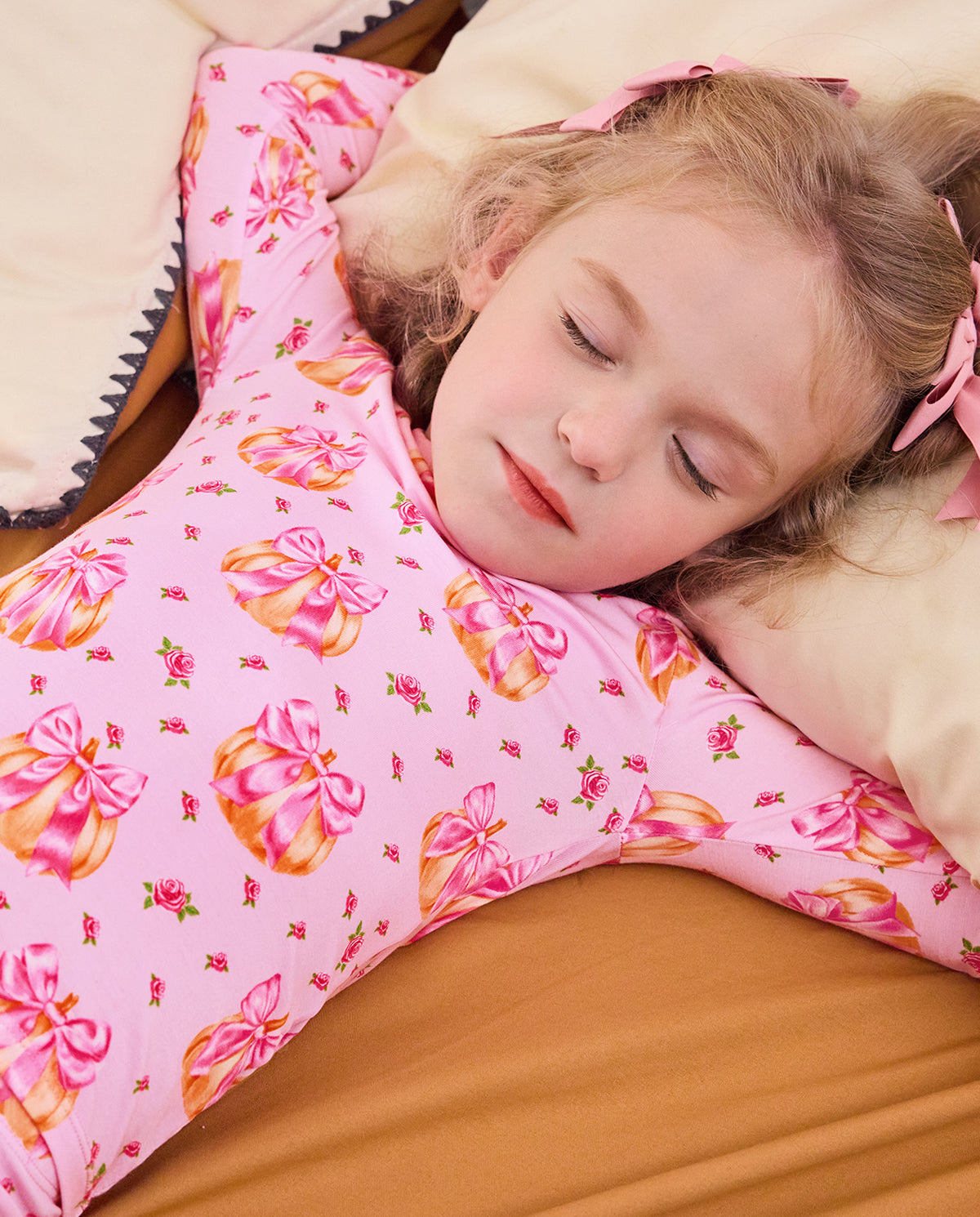 Child reclining on bedding in the Pumpkin Bows two-piece pajama set.