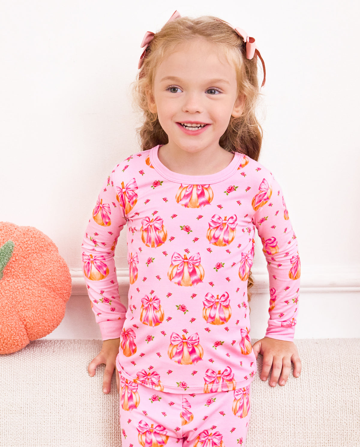 Front view of a child seated on a sofa in Pumpkin Bows pajamas.