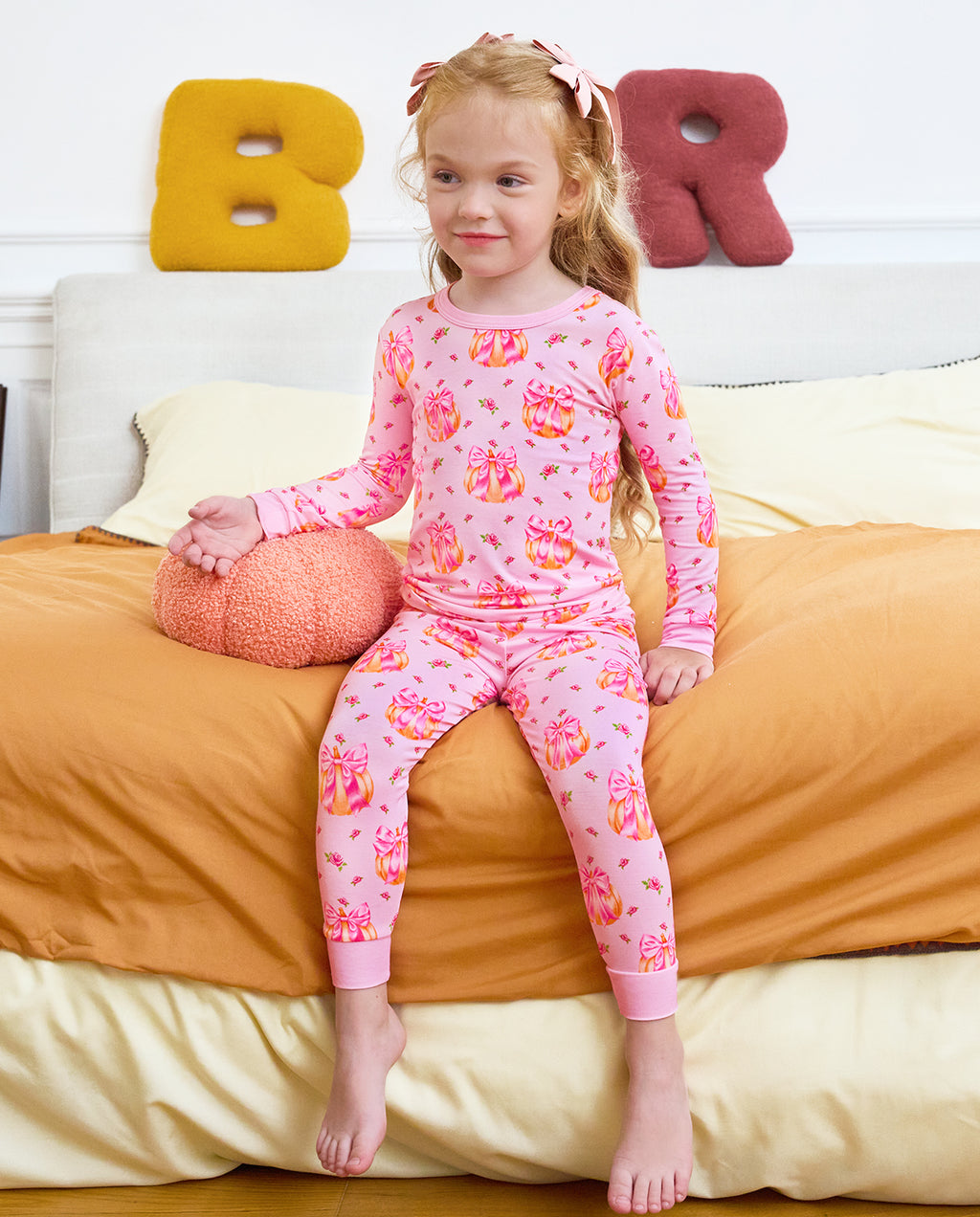 Full front view of a child seated on a sofa in Pumpkin Bows pajamas.