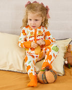 Child seated on a sofa in the cream Pumpkin Patch zip-up romper with orange cuffs.