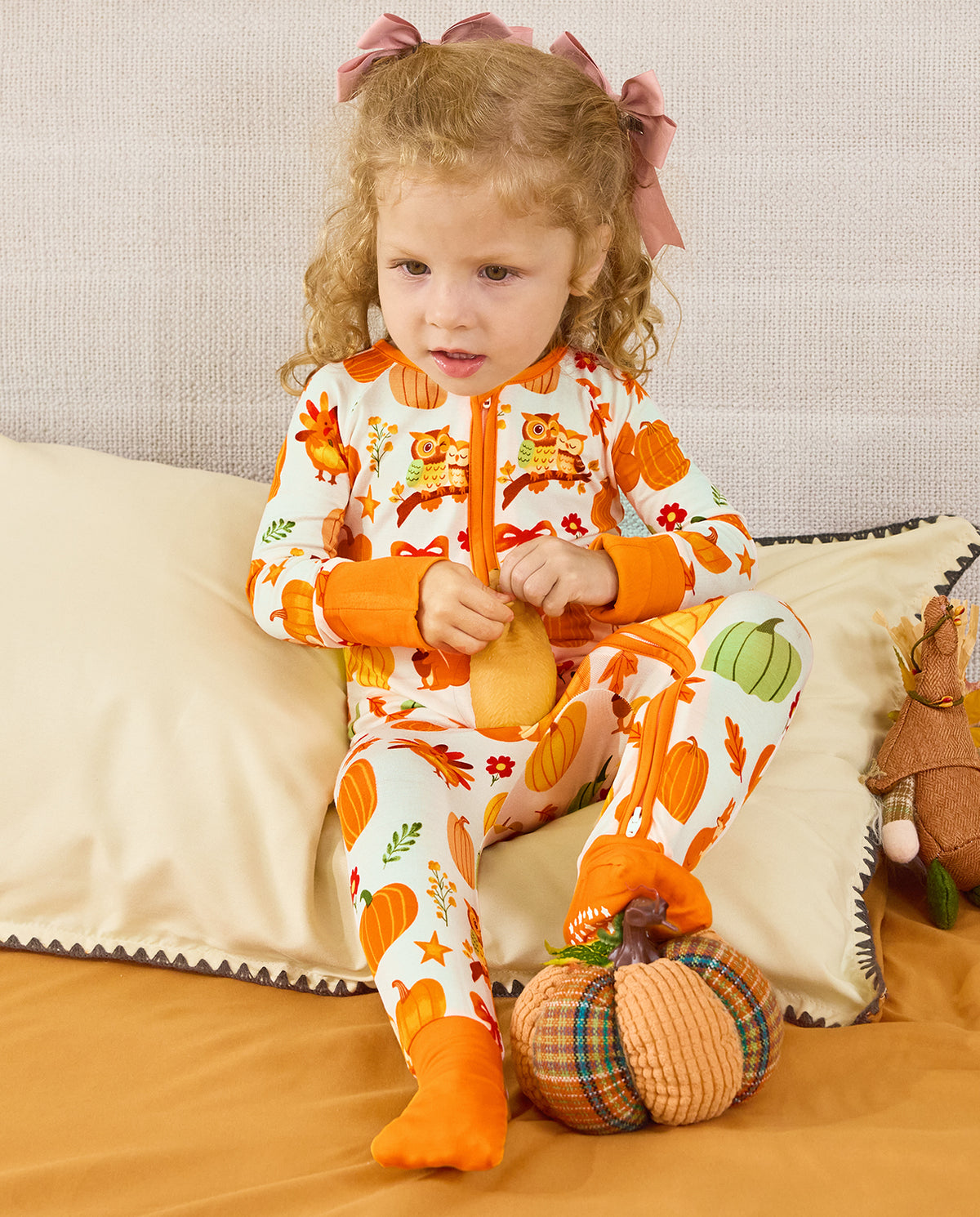 Child seated on a sofa in the cream Pumpkin Patch zip-up romper with orange cuffs.