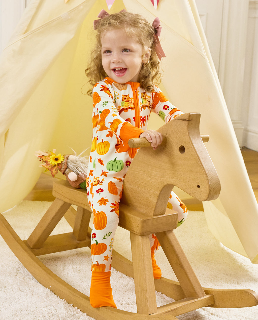 Child standing beside a wooden rocking horse in the Pumpkin Patch romper.
