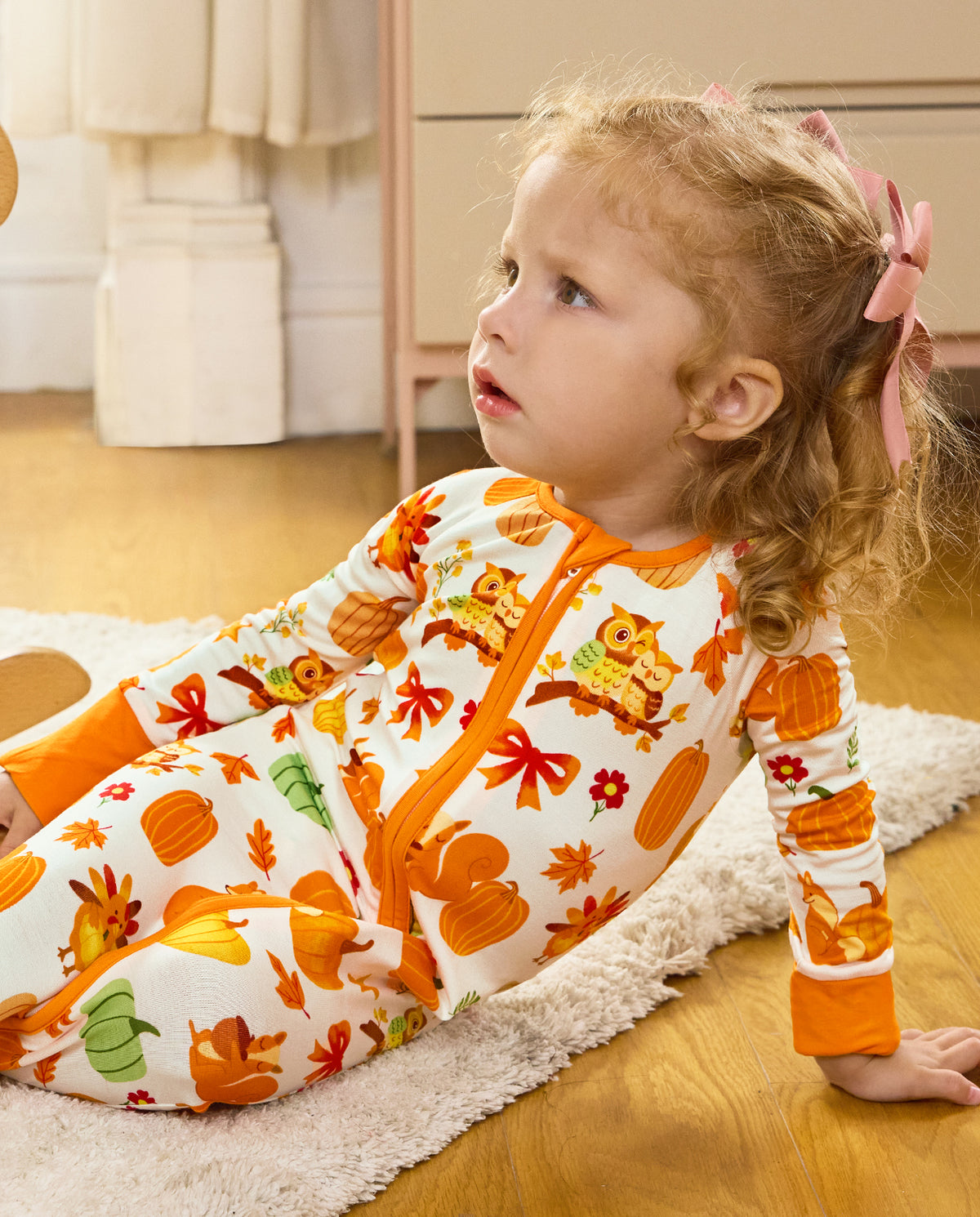 Child reclining on a rug and looking upward in the Pumpkin Patch romper.
