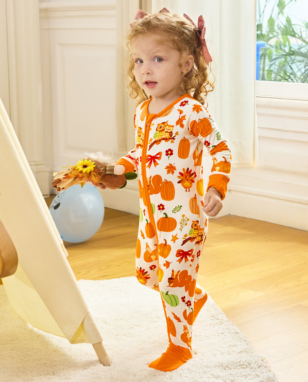 Child standing and holding autumn leaves in the Pumpkin Patch romper.