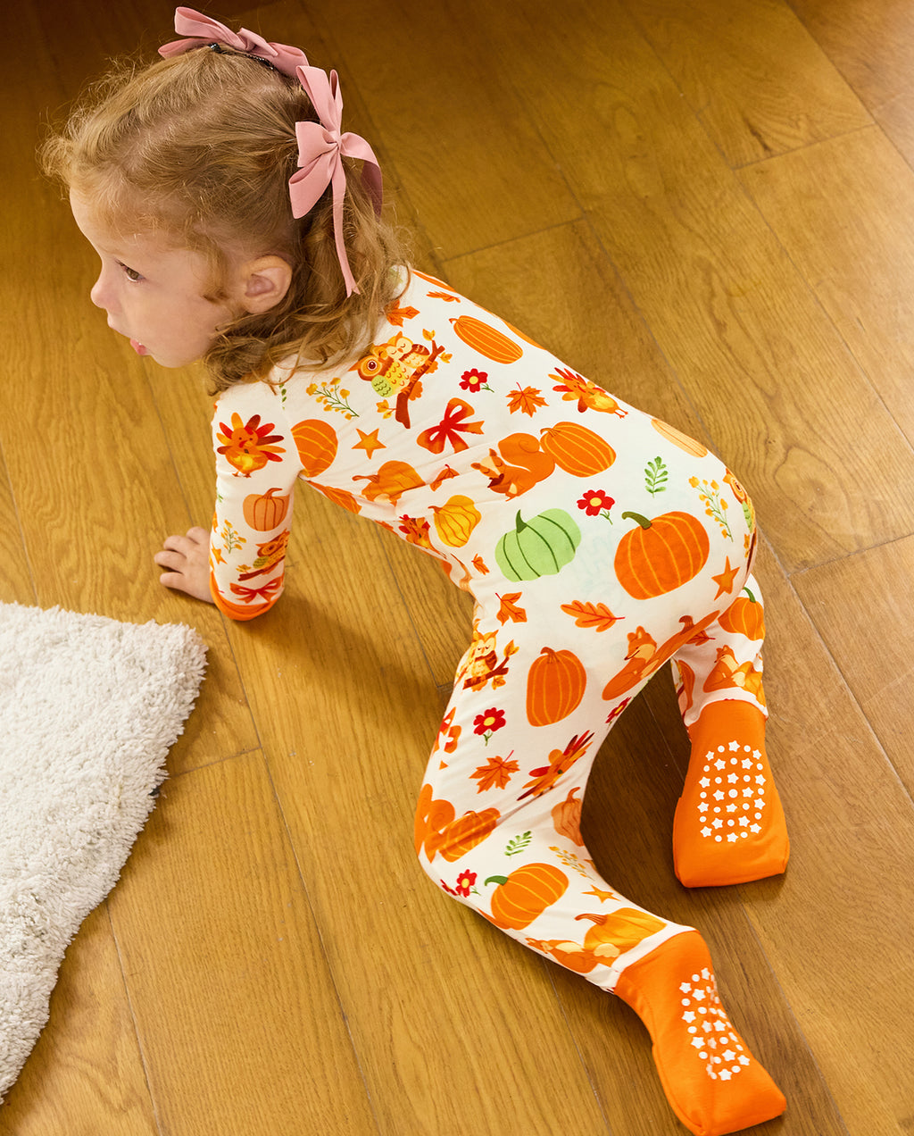 Rear view of a child crawling on a wooden floor, showing orange foot cuffs and white sole grips.